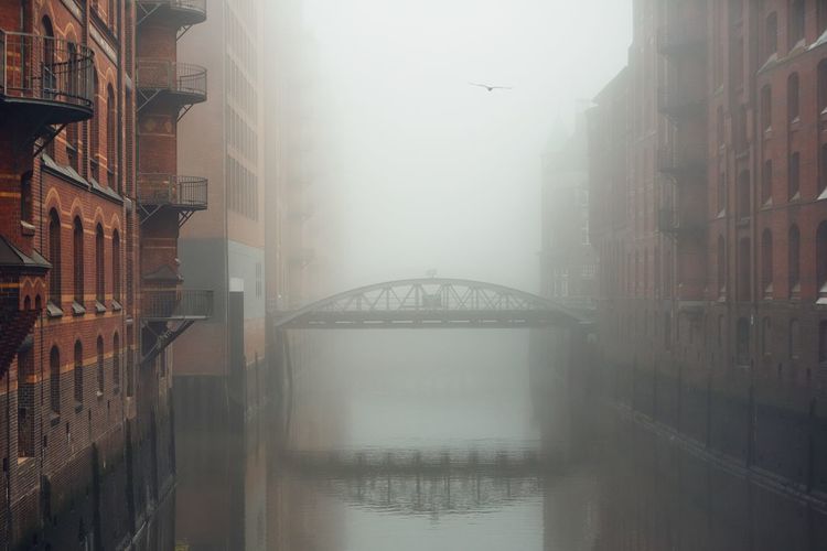 Bridge over canal amidst buildings during foggy weather