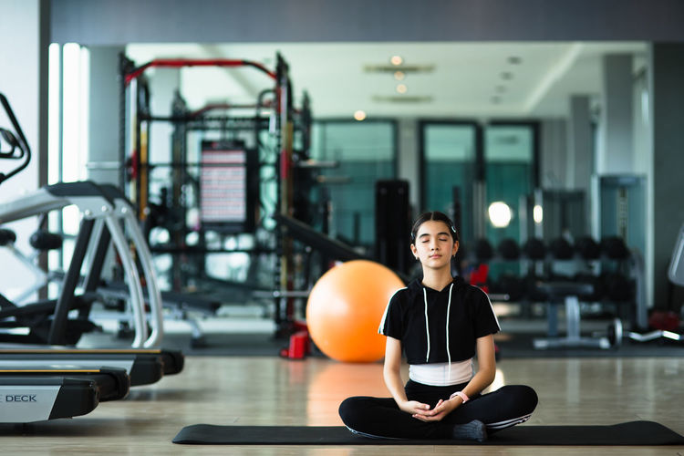 Full length of girl meditating at gym