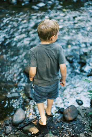 Rear view of boy standing on rock in forest