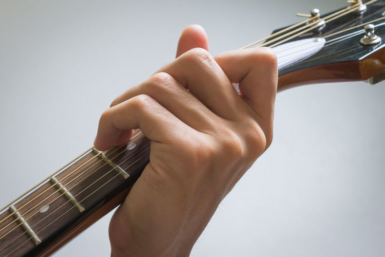 Close-up of hand holding guitar against white background