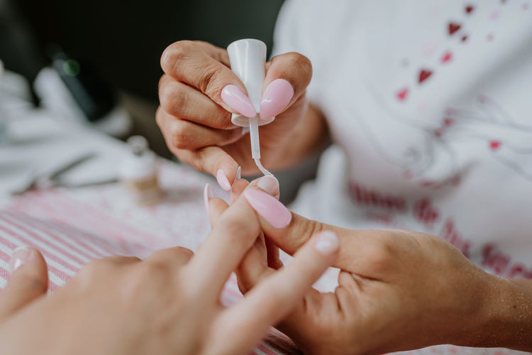 High angle of unrecognizable female artist applying nail polish on fingernails of client during manicure in beauty studio