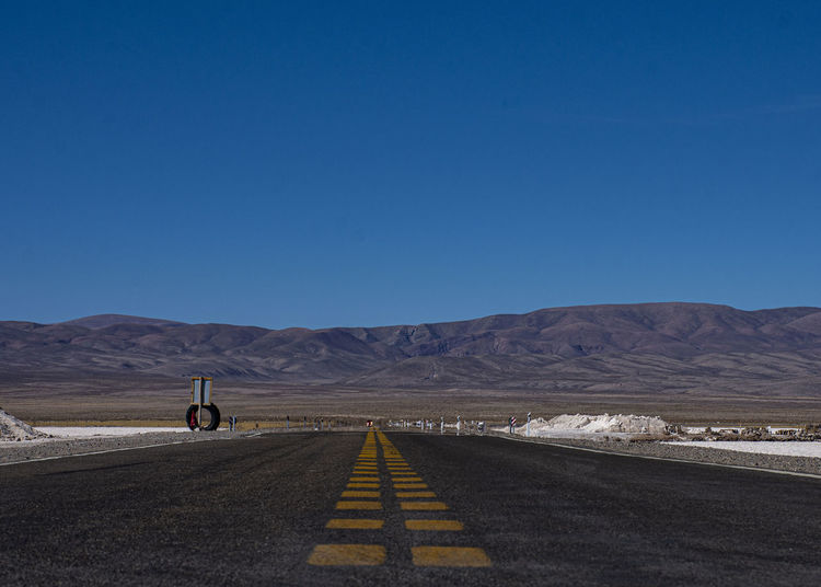 Road leading towards mountains against clear blue sky