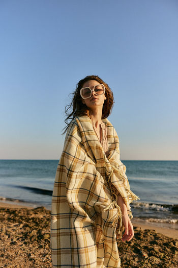Young woman standing at beach against clear blue sky