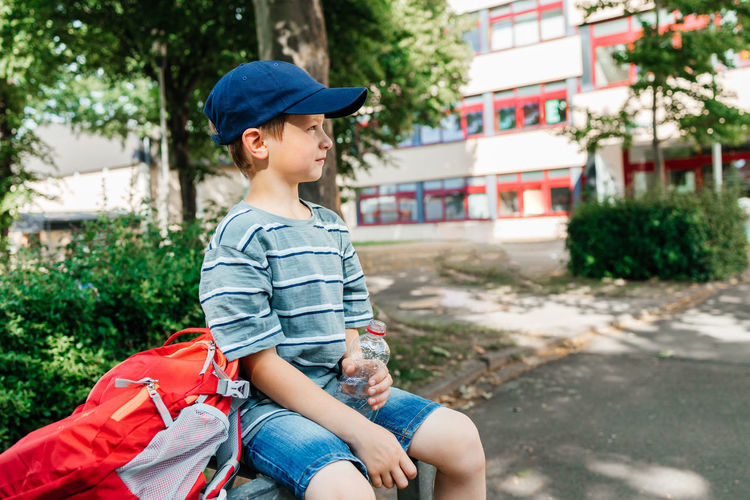 A schoolboy sits on a bench in the school yard and drinks water from a bottle. water balance 