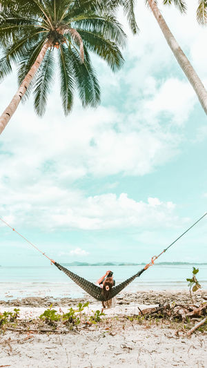 Rear view of woman relaxing on hammock at beach
