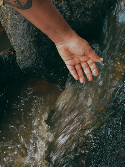 Cropped hand of woman touching stream flowing on rock