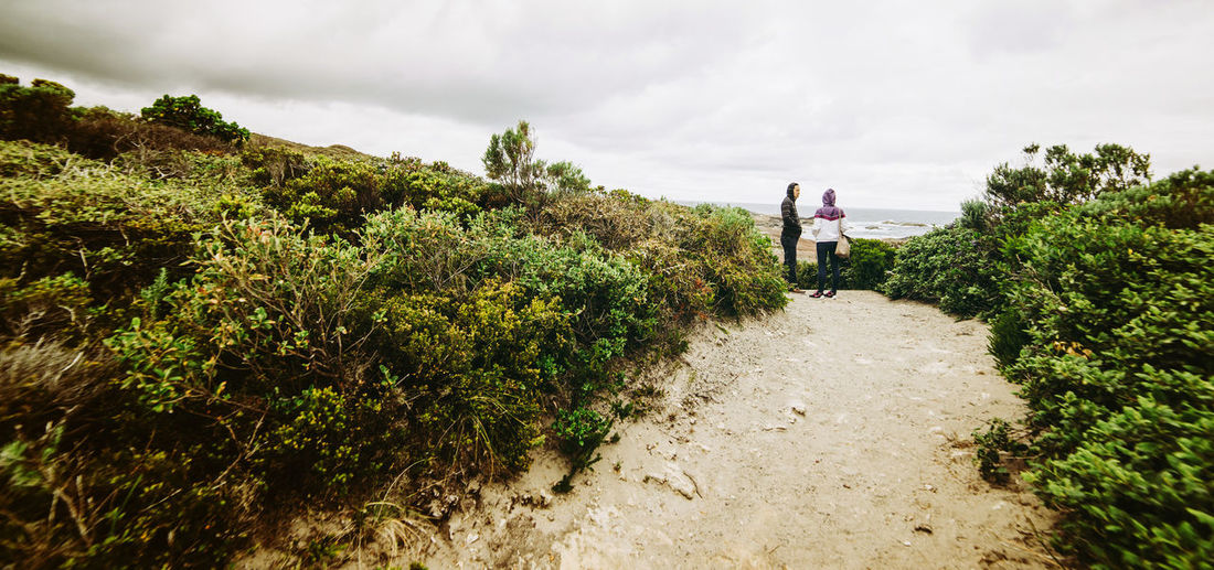Couple standing at beach against cloudy sky