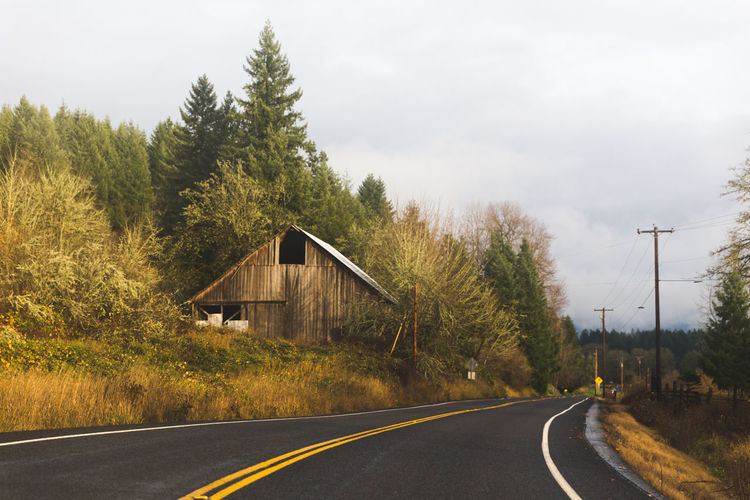 Old farm building among forest trees on a rural two-lane road or highway.