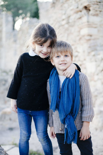 Portrait of siblings standing against stone wall