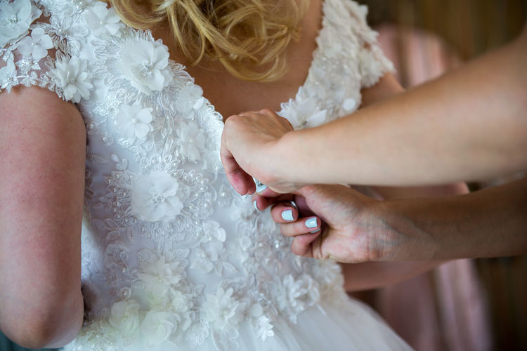 Cropped hands of woman helping bride in getting dressed