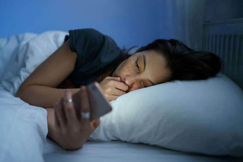 Anxious woman in bed using smartphone at night, can not stop scrolling social media before bedtime