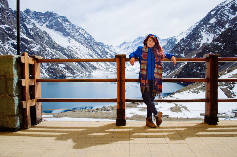 Woman standing on railing against snowcapped mountains during winter