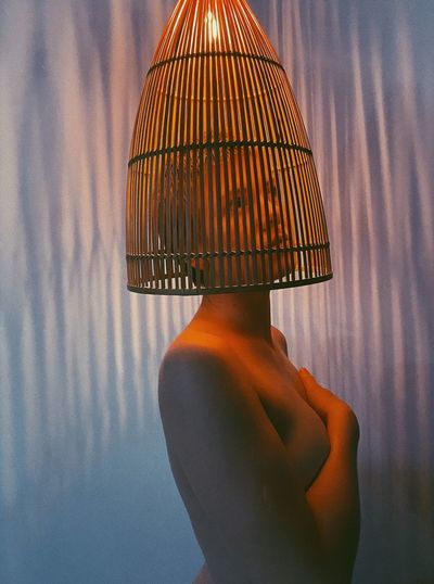 Sensuous shirtless woman with hands covering breasts standing under lighting equipment against wall