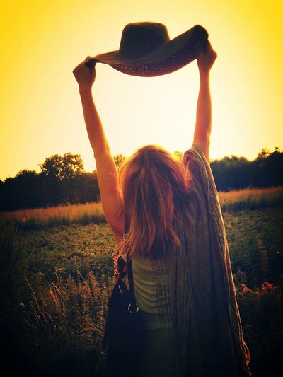 Rear view of woman with arms raised standing against sky during sunset