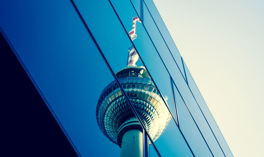 Reflection of television tower in modern building against blue sky