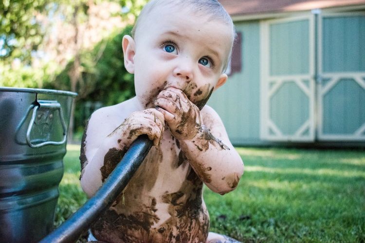 Close-up of dirty boy holding pipe in mouth while sitting on field