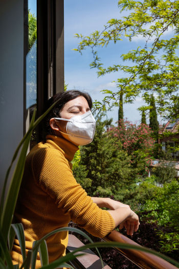 Woman wearing mask standing by window at home