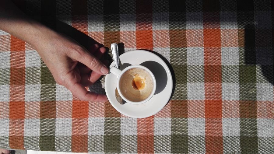 Cropped hand holding coffee cup on table during sunny day