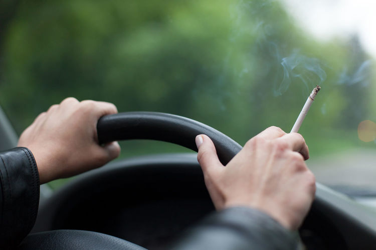 Cropped hands of woman holding cigarette while traveling in car