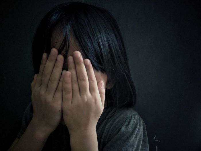 Close-up of sad girl covering face against black background
