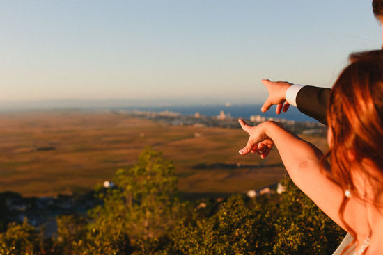 Cropped hand of couple pointing against sky