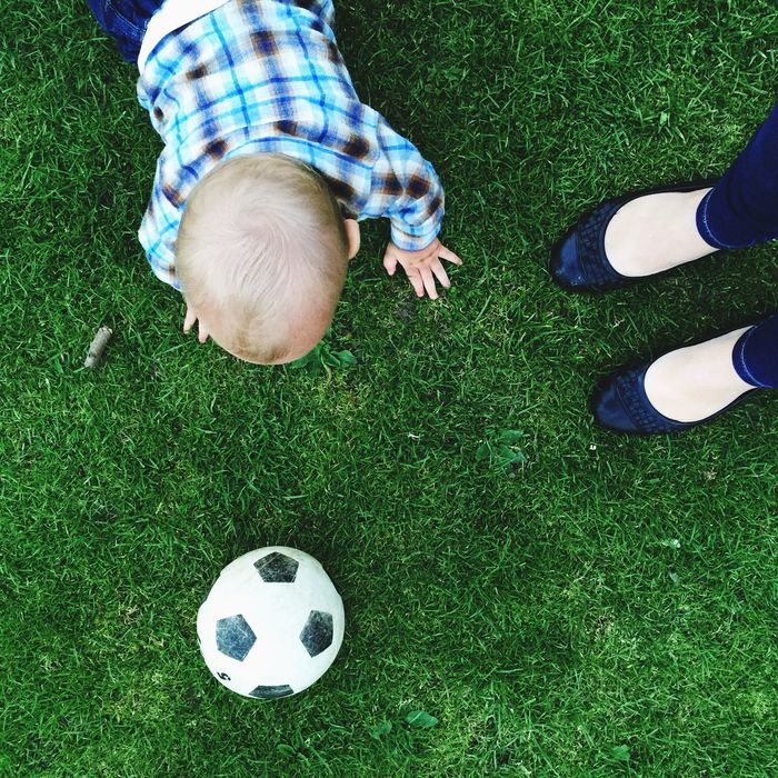 Low section of mother with son playing soccer on grassy field