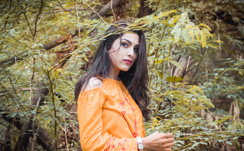Portrait of beautiful young woman standing against plants