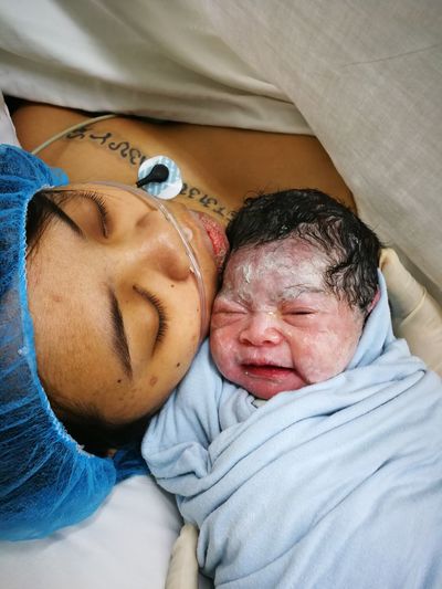 Close-up of mother with baby girl sleeping on bed at hospital