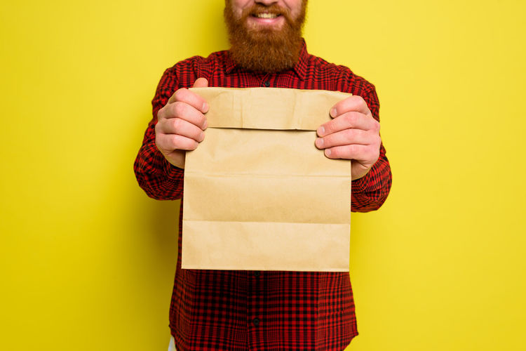 Midsection of man holding paper against yellow background
