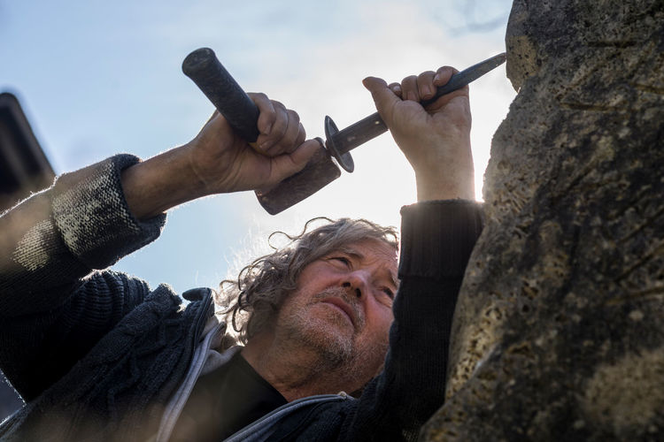 Low angle view of man carving on rock against sky