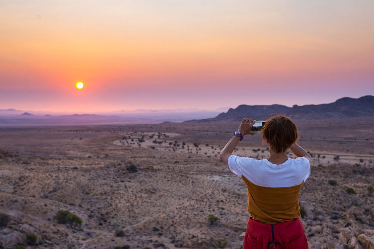 Rear view of woman photographing sunset