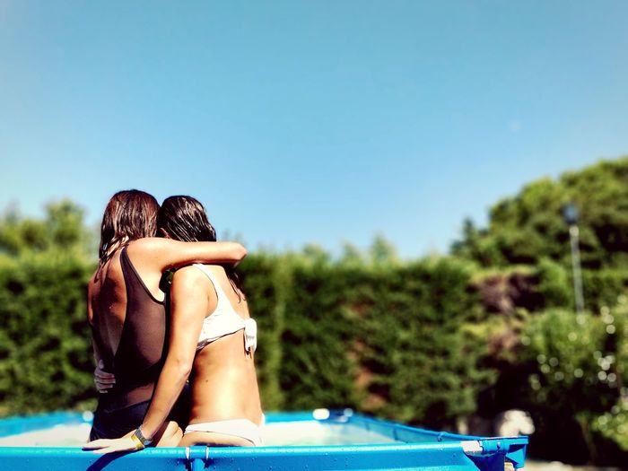 Friends embracing in wading pool at back yard on sunny day