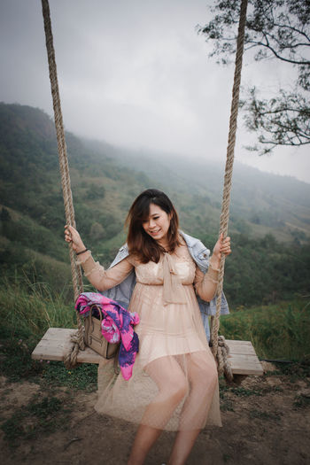 Smiling woman sitting on swing against mountain range