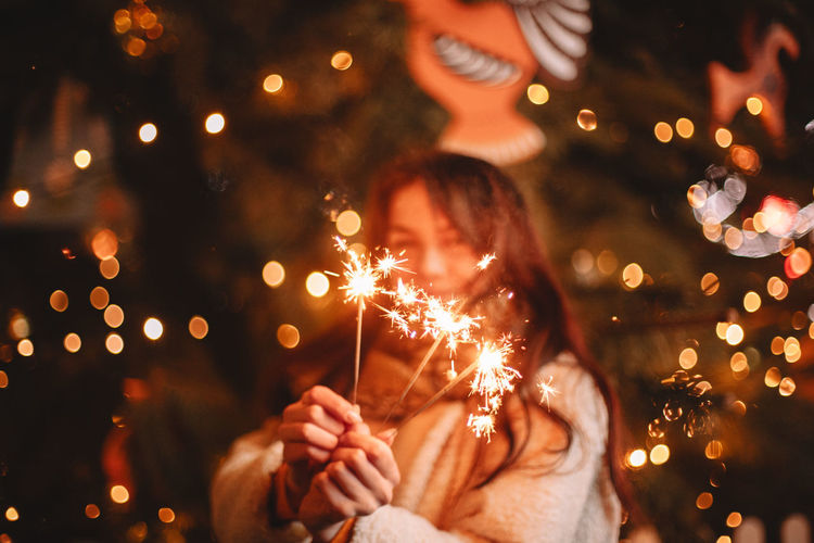 Midsection of woman holding sparkler at night