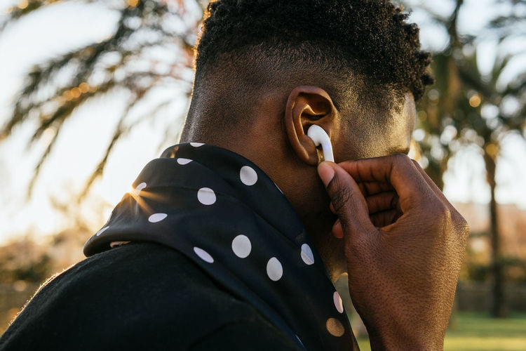 Side view of anonymous black guy adjusting true wireless earbuds while listening to music in park
