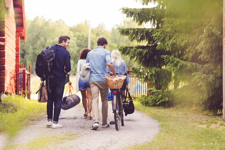 Rear view of friends walking with bicycle and luggage on footpath by trees