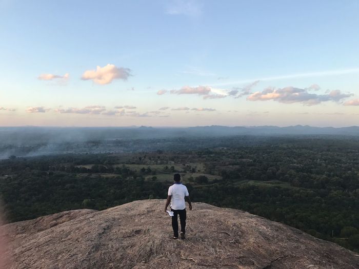 Rear view of man standing on mountain against sky