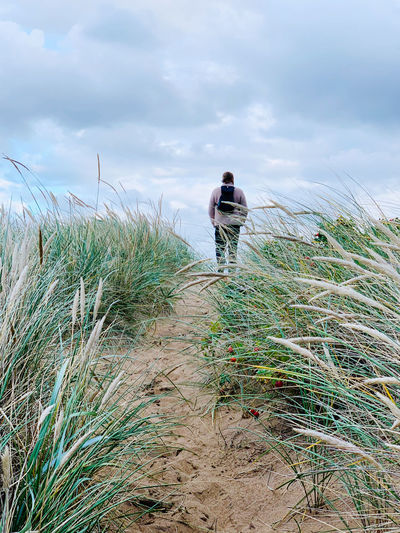 Rear view of man walking on field against sky