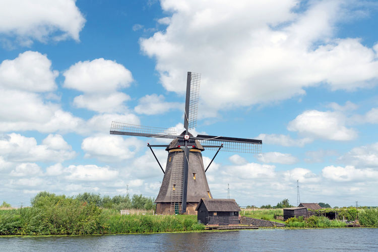 Traditional windmill by river against sky