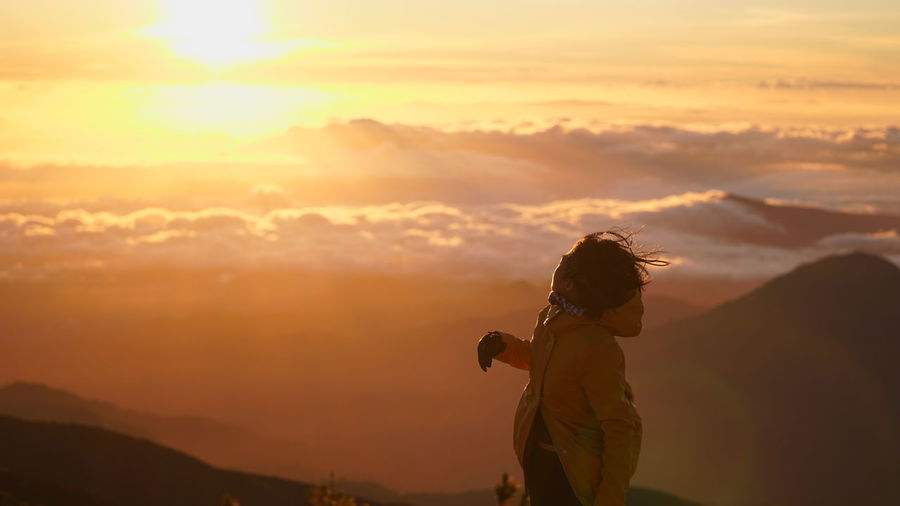 Woman standing on mountain against sky during sunset
