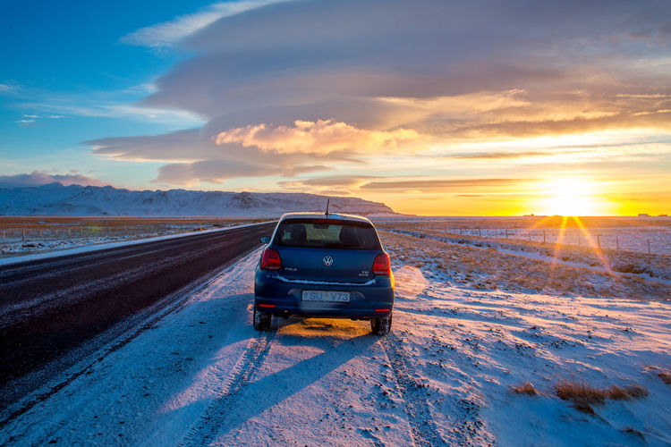 Car on snow covered field against sky during sunset