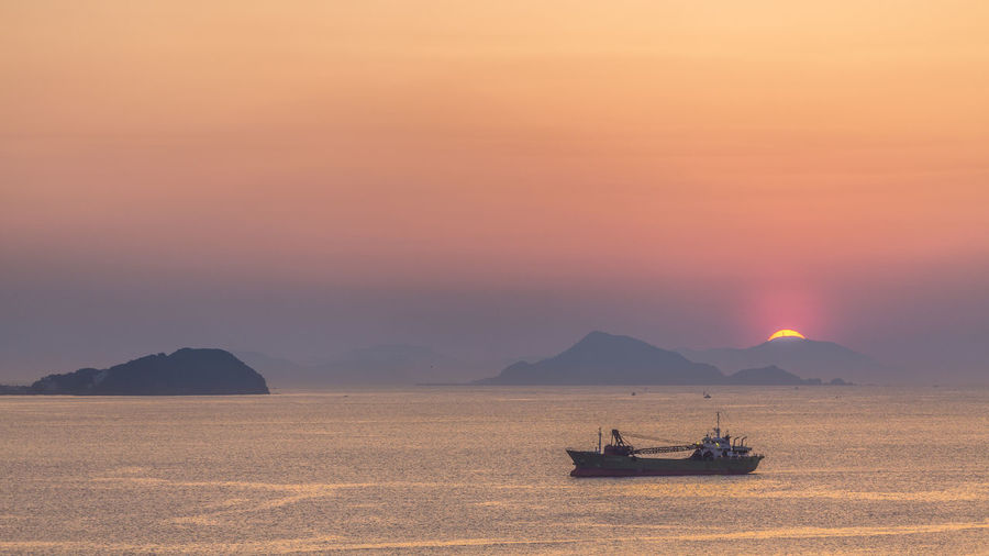 Boat sailing in sea against sky during sunset