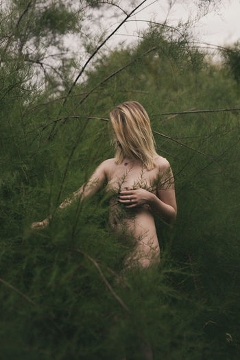 Naked woman standing amidst plants