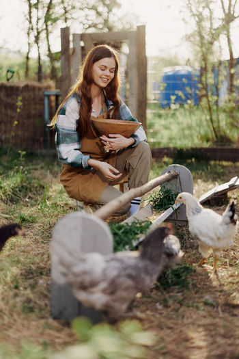 Smiling woman feeding hen in farm