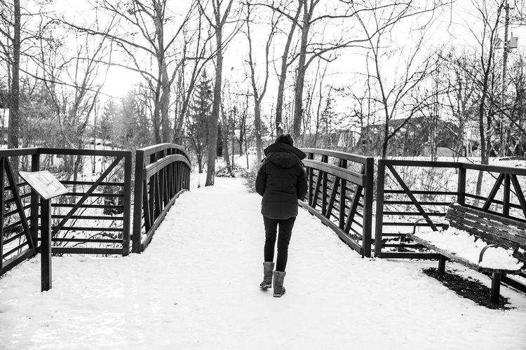 Rear view of man standing on snow covered footbridge