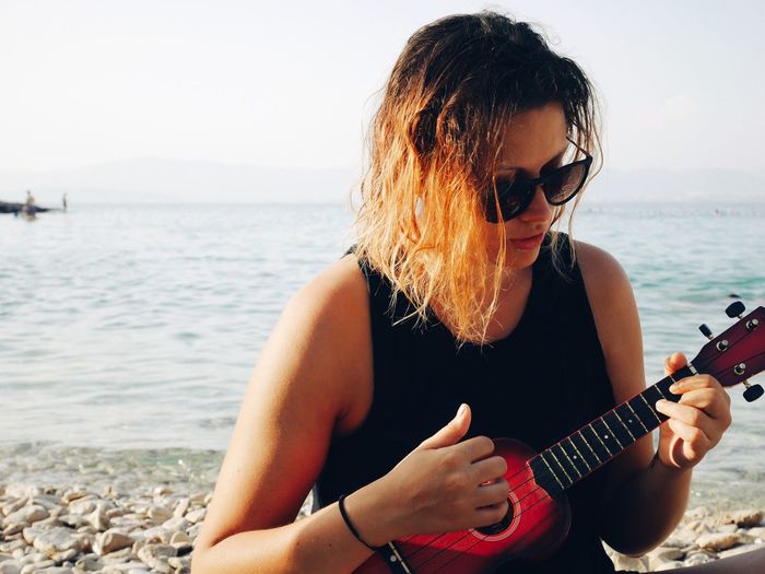 Portrait of woman playing guitar at beach against sky