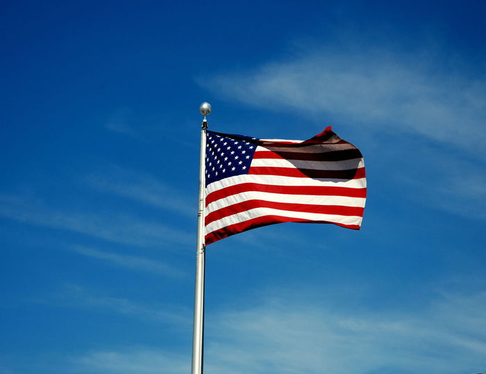 Low angle view of american flag waving against sky