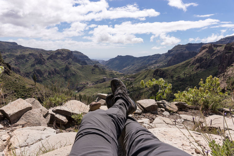 Low section of person relaxing on mountain against sky