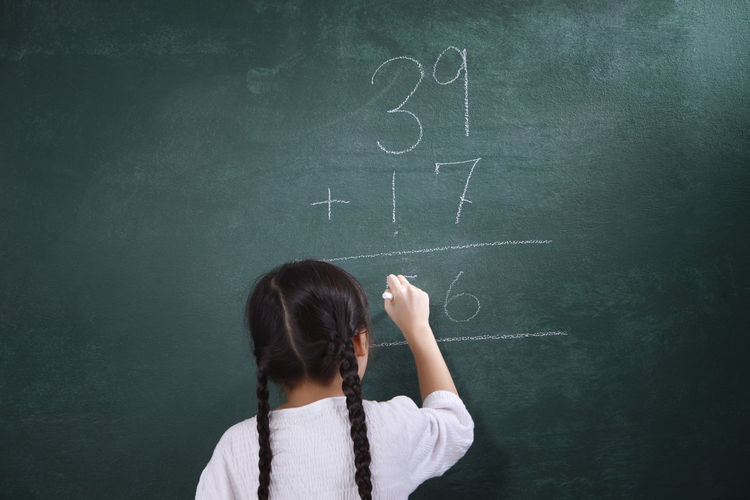 Rear view of girl learning mathematics on blackboard