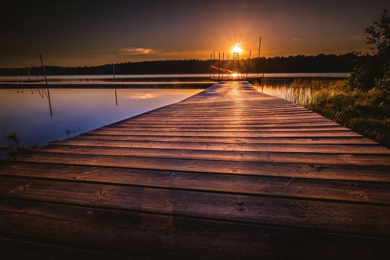 Pier over lake against sky at sunset